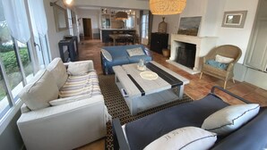 A spacious living area with a sofa set, a coffee table, and a hanging light fixture. There is a fireplace and a dining area in the background. - ALIZE              . (Rivedoux-Plage)