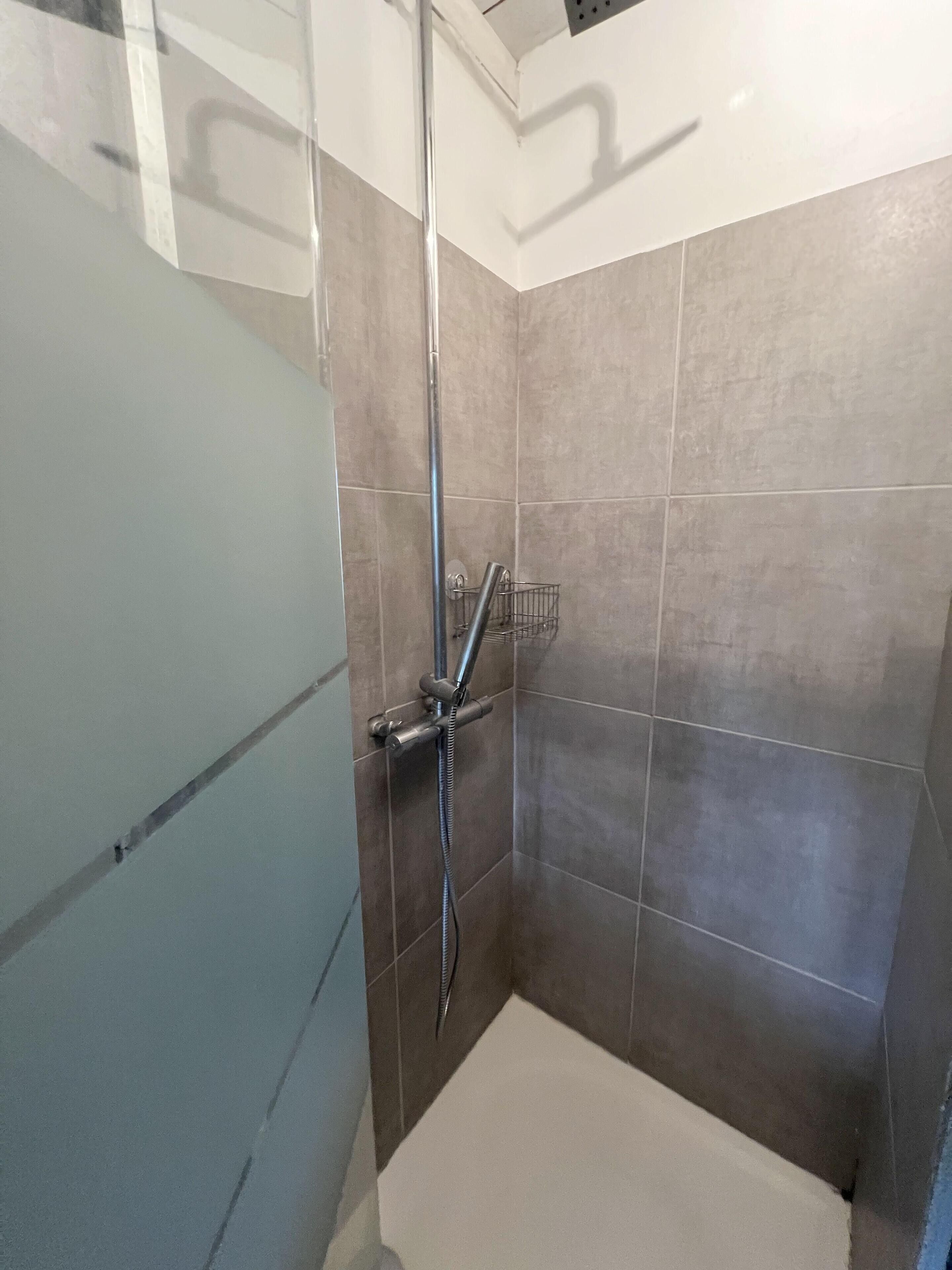 A small, tiled shower area with a glass door and a metal showerhead.