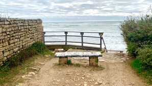Un muro de piedra, un banco de madera y una barandilla de metal con vistas al mar.