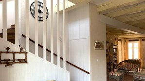 Una escalera con paredes blancas y barandilla de madera que conduce a una sala de estar con sofá, sillón y una mesa.
