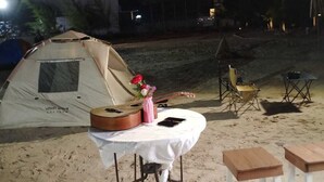 Una tienda de campaña montada en una playa arenosa con una mesa y sillas cerca.