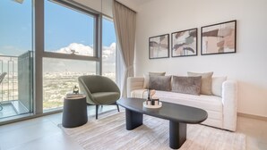 Una sala de estar moderna con un sofá blanco, una mesa de centro negra y un sillón verde. Hay tres cuadros abstractos en la pared y un ventanal con vistas a la ciudad.