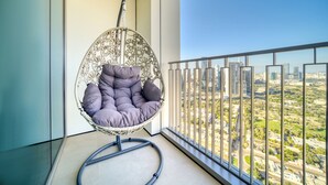 Una silla colgante con asiento y respaldo acolchados, ubicada en un balcón con vistas a la ciudad.