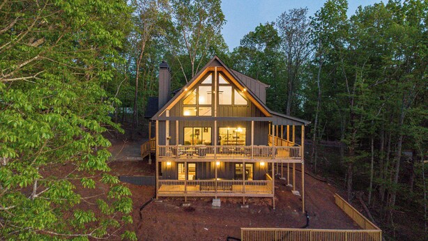 A two-story log cabin with a balcony, surrounded by trees.