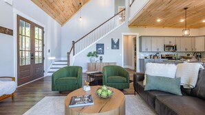 A spacious living area with a wooden ceiling, a staircase, and a kitchen in the background.