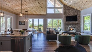 A spacious living area with a stone fireplace, wooden ceiling, and large windows.