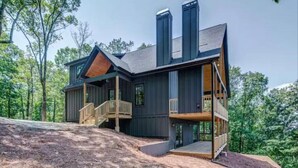 A modern two-story house with a wooden deck and a staircase leading to a second-floor balcony.