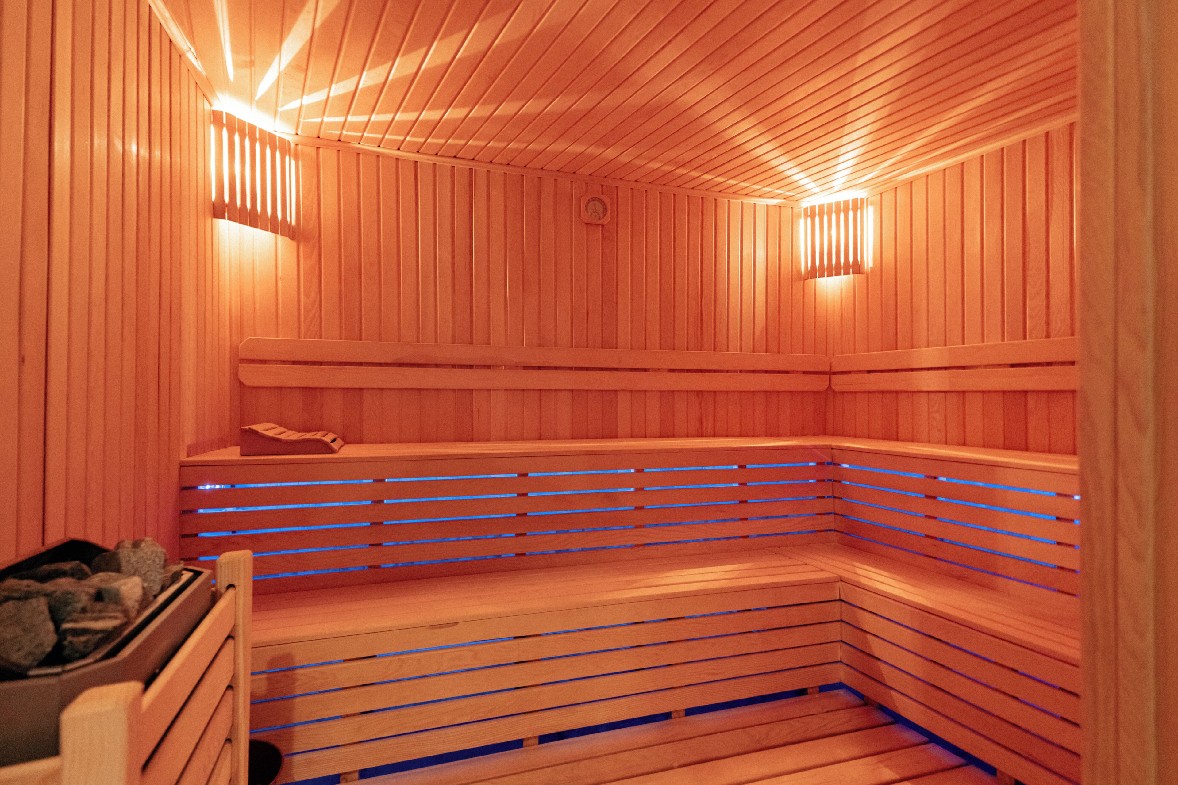 A sauna with wooden slats and benches, a bench with a towel, and a small heater on the wall.