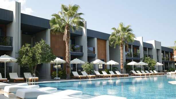 Un hotel moderno con area piscina, lettini e ombrelloni.