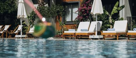 A pool with lounge chairs and umbrellas, surrounded by plants and a building with wooden paneling.
