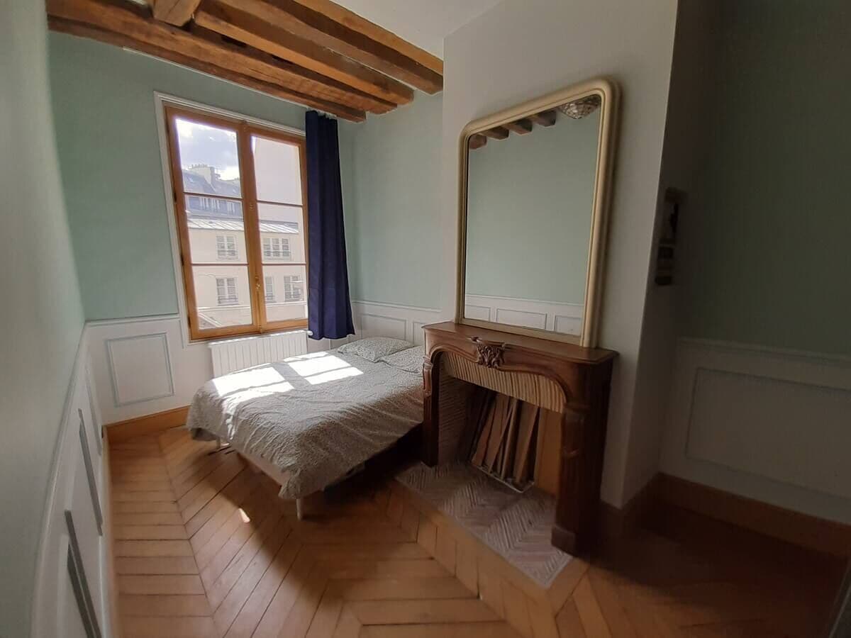 A bedroom with a bed, a wooden dresser, a mirror, and a window with curtains.