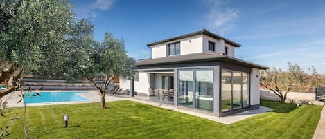 A modern house with a pool, a well-maintained lawn, and a clear blue sky.