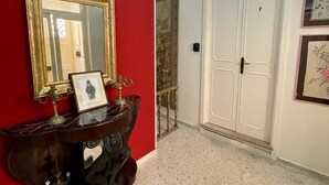 Un pasillo con pared roja, una consola de madera oscura con espejo y un cuadro enmarcado, y una puerta blanca con el número 7.