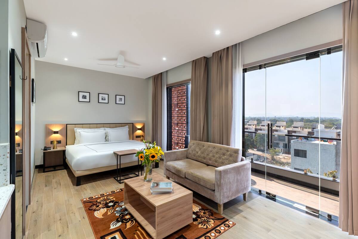 Ein modernes Hotelzimmer mit einem großen Bett, einer Couch, einem Couchtisch und Blick auf die Stadt durch große Fenster.