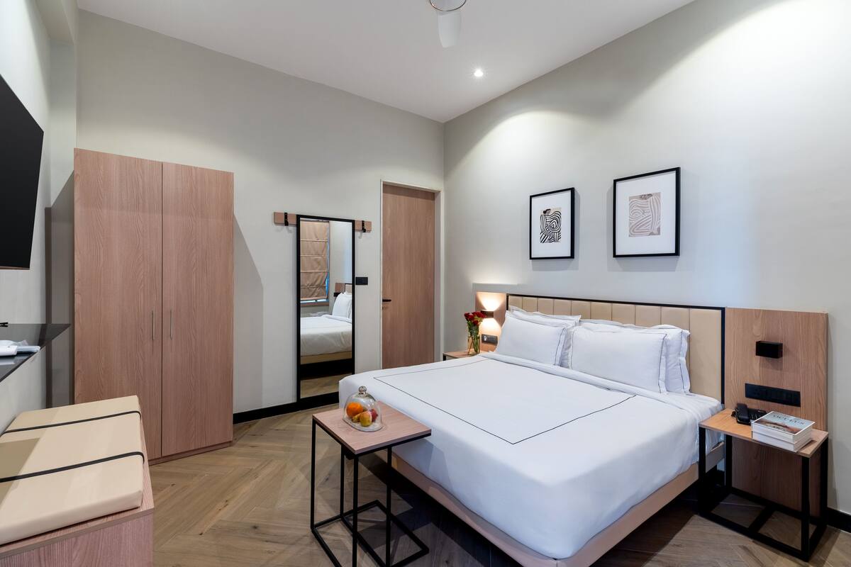 Ein modernes Hotelzimmer mit einem großen Bett, Nachttischen, einem Kleiderschrank und gerahmten Kunstwerken an der Wand.