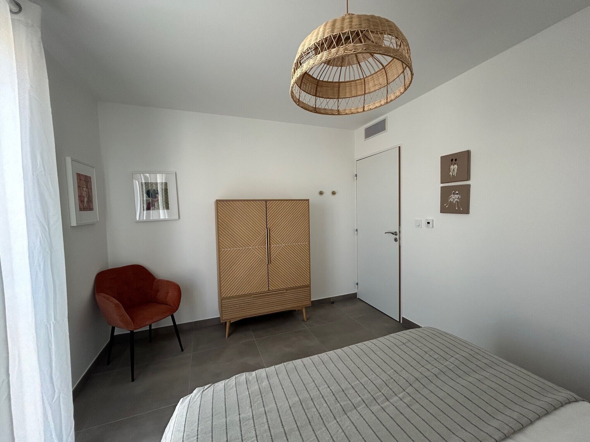 A bedroom with a bed, a red chair, a wardrobe, and a hanging light fixture.