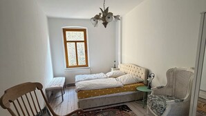 A bedroom with a bed, a rocking chair, a chair, a window, and a chandelier. - Lilienstein (Königstein)