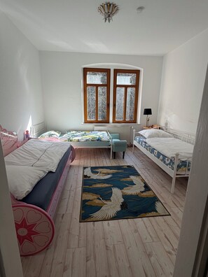 Une chambre avec deux lits, une fenêtre, un radiateur et un plancher en bois.