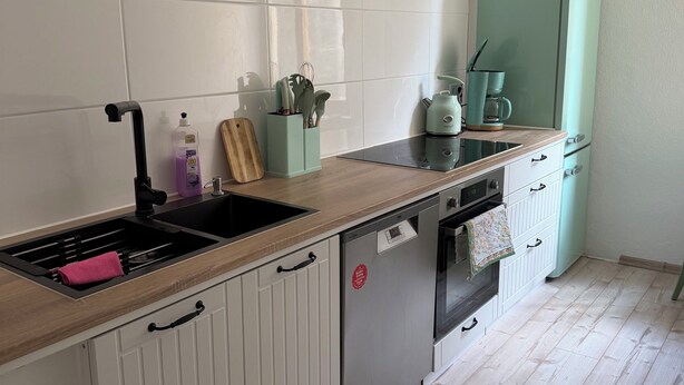 A kitchen with white cabinets, a black sink, a green coffee maker, and a dishwasher. - Lilienstein (Königstein)