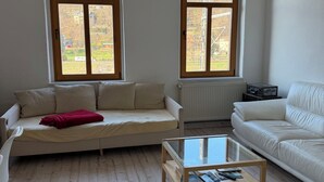 A living room with two sofas, a glass coffee table, a chandelier, and large windows. - Lilienstein (Königstein)