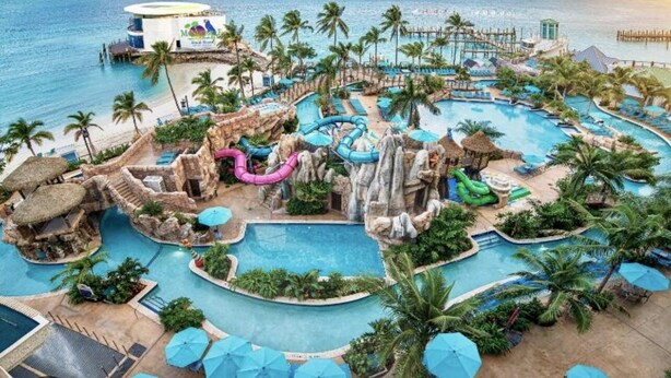 Een resort met meerdere zwembaden, glijbanen en een strandgedeelte.