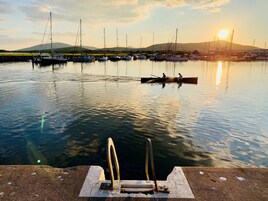 A marina with boats docked at the pier, a sunset in the background, and a concrete structure with metal rings in the foreground.