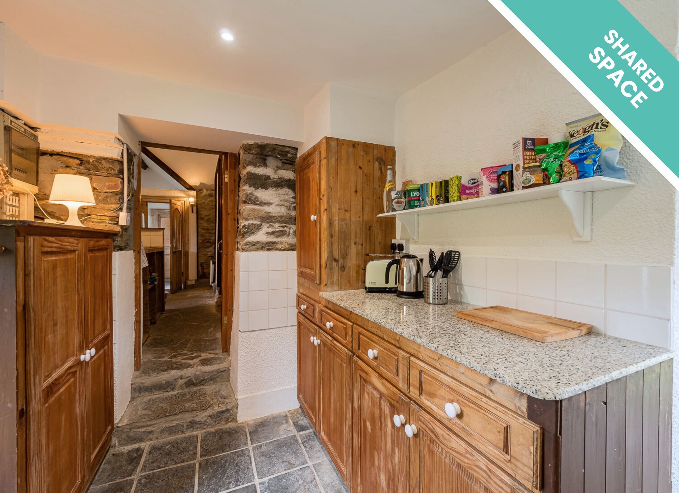 Una cocina con armarios de madera, encimera de granito y pared de piedra.