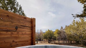 Un jacuzzi con un muro de madera y vistas a árboles y colinas al fondo.