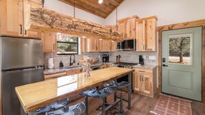 Una cocina con armarios de madera, un refrigerador de acero inoxidable, una isla de madera con taburetes de bar y una puerta verde.