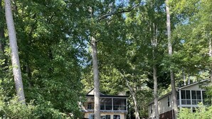 Une terrasse en bois mène à un chalet doté d’une grande fenêtre, le tout étant entouré d’arbres.