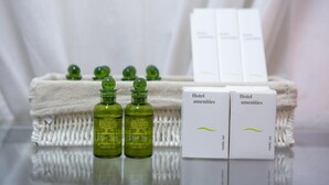 Bottles of Olive Tree shampoo and conditioner, two sets of Hotel amenities, and a white towel. - Sleep in Style, Wake up in the Center of it All! (Thessaloniki)