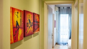 A hallway with three abstract paintings on the wall and a door leading to a room with a window. - Sleep in Style, Wake up in the Center of it All! (Thessaloniki)