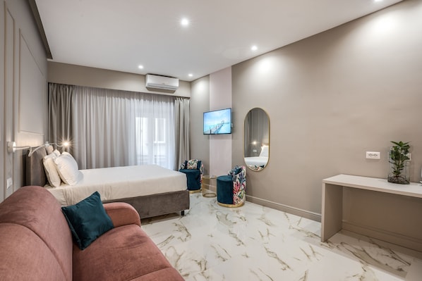 A modern hotel room with a bed, a sofa, a TV, a mirror, and a desk.