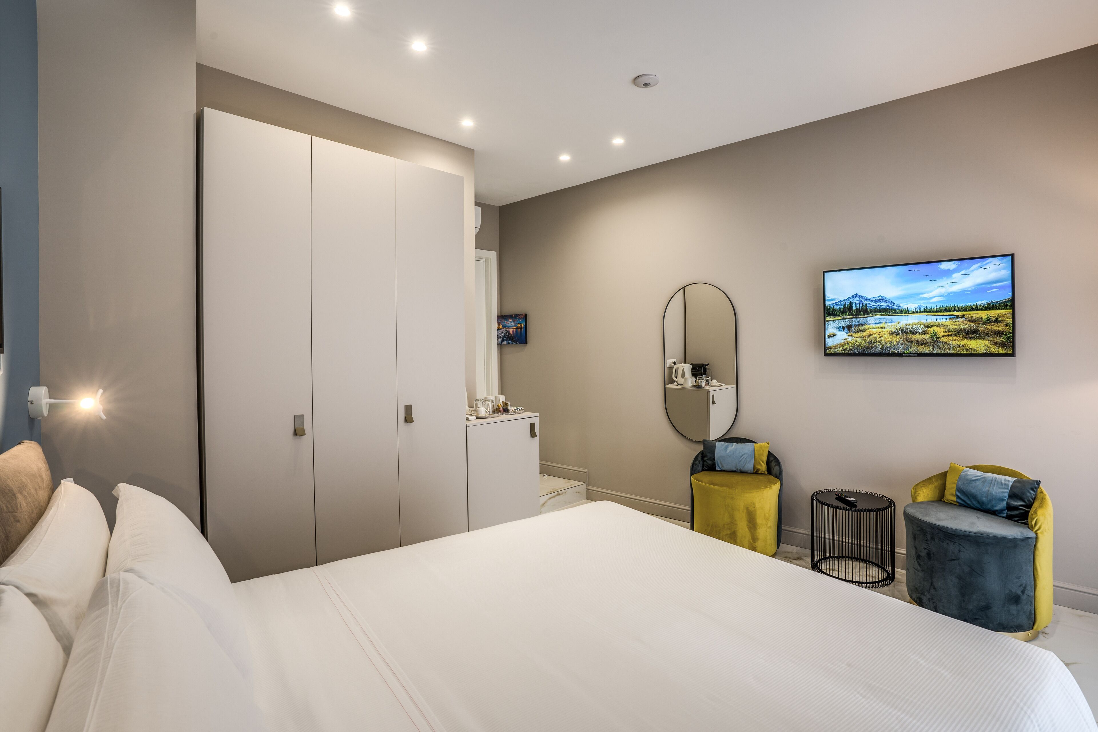 A modern bedroom with a large bed, a wardrobe, a mirror, a television, and two small side tables.