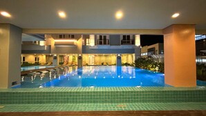 A swimming pool with a tiled floor and a surrounding area with lounge chairs and a building with multiple levels. - Saint Honore Condo (Iloilo)