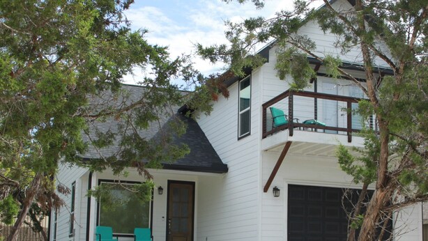 Ein zweistöckiges Haus mit Balkon, Garage und überdachter Veranda mit Sitzgelegenheiten.