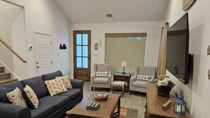 Ein Wohnzimmer mit einem dunklen Sofa, zwei Sesseln, einem Couchtisch und einem Fernseher.