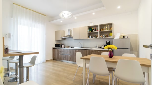 A modern kitchen with a dining area, featuring a wooden table, white chairs, and a vase of yellow flowers. - Boutique B&B in Pompeii - Stay & Local Experiences (Pompei)