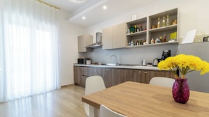 A modern kitchen with wooden cabinets, a built-in stove, and a coffee maker. There is a dining table with chairs and a vase of yellow flowers. - Boutique B&B in Pompeii - Stay & Local Experiences (Pompei)