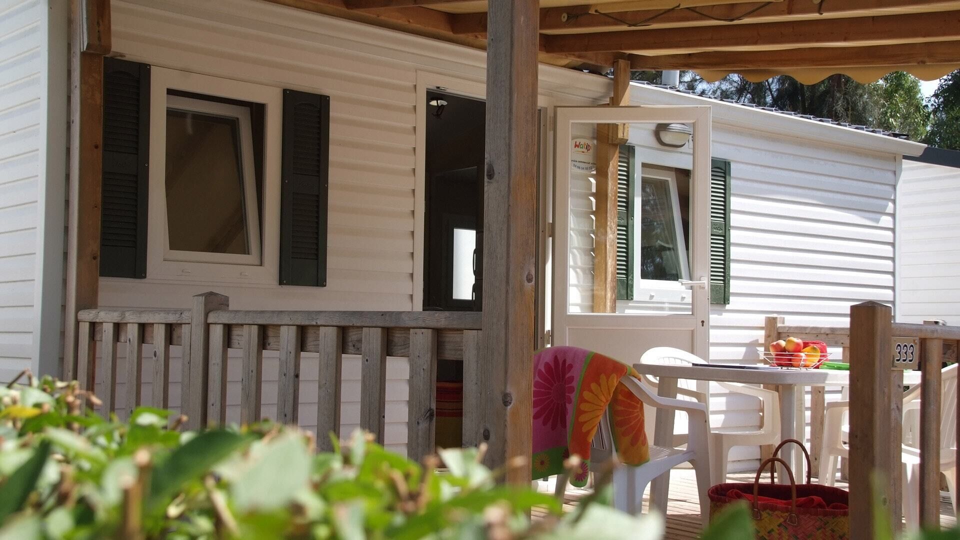 Ein Wohnmobil mit Veranda, einem Tisch mit Stühlen und einem kleinen Garten.