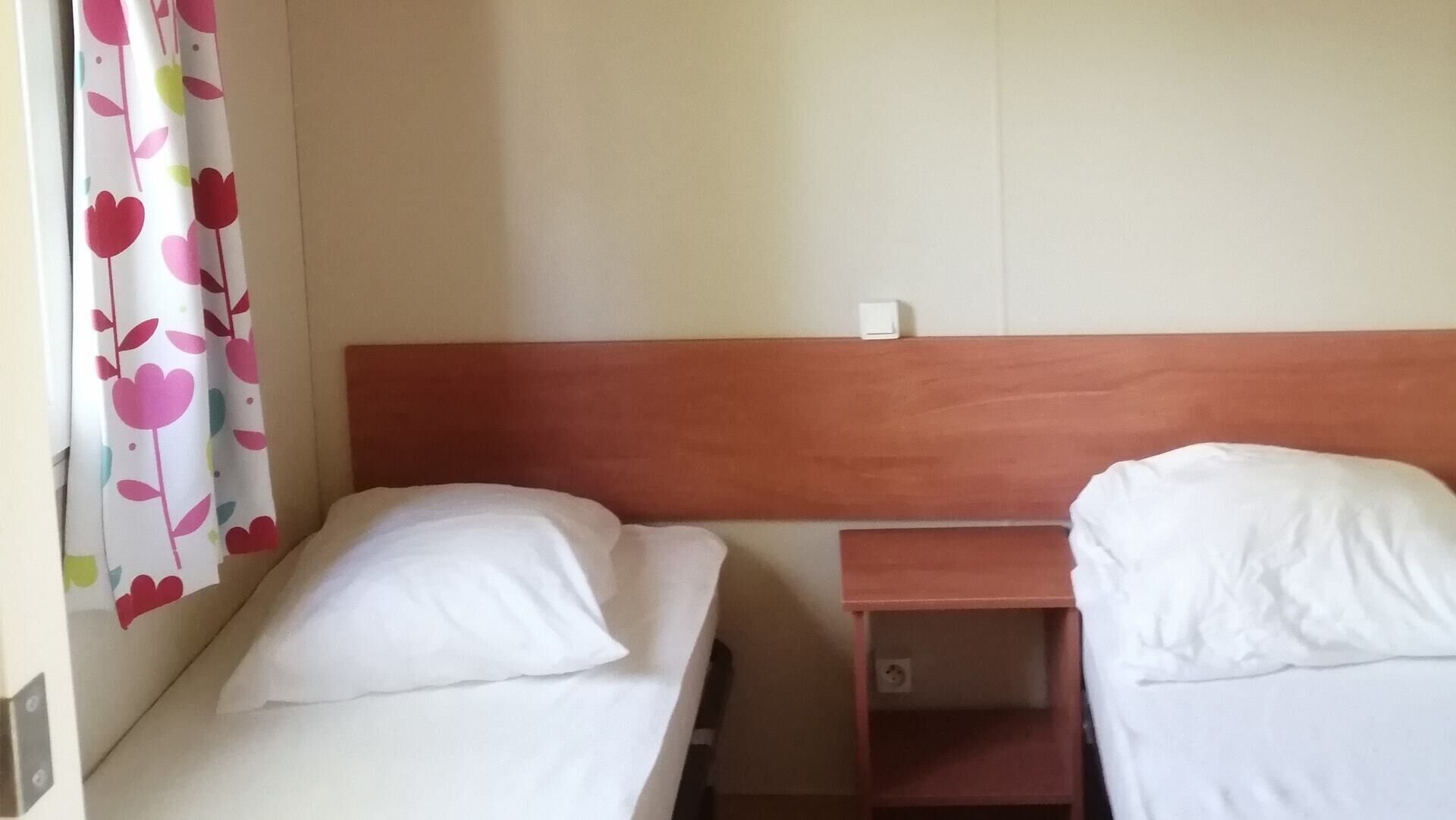 Une chambre simple avec deux lits simples, une tête de lit en bois et une petite table de chevet.