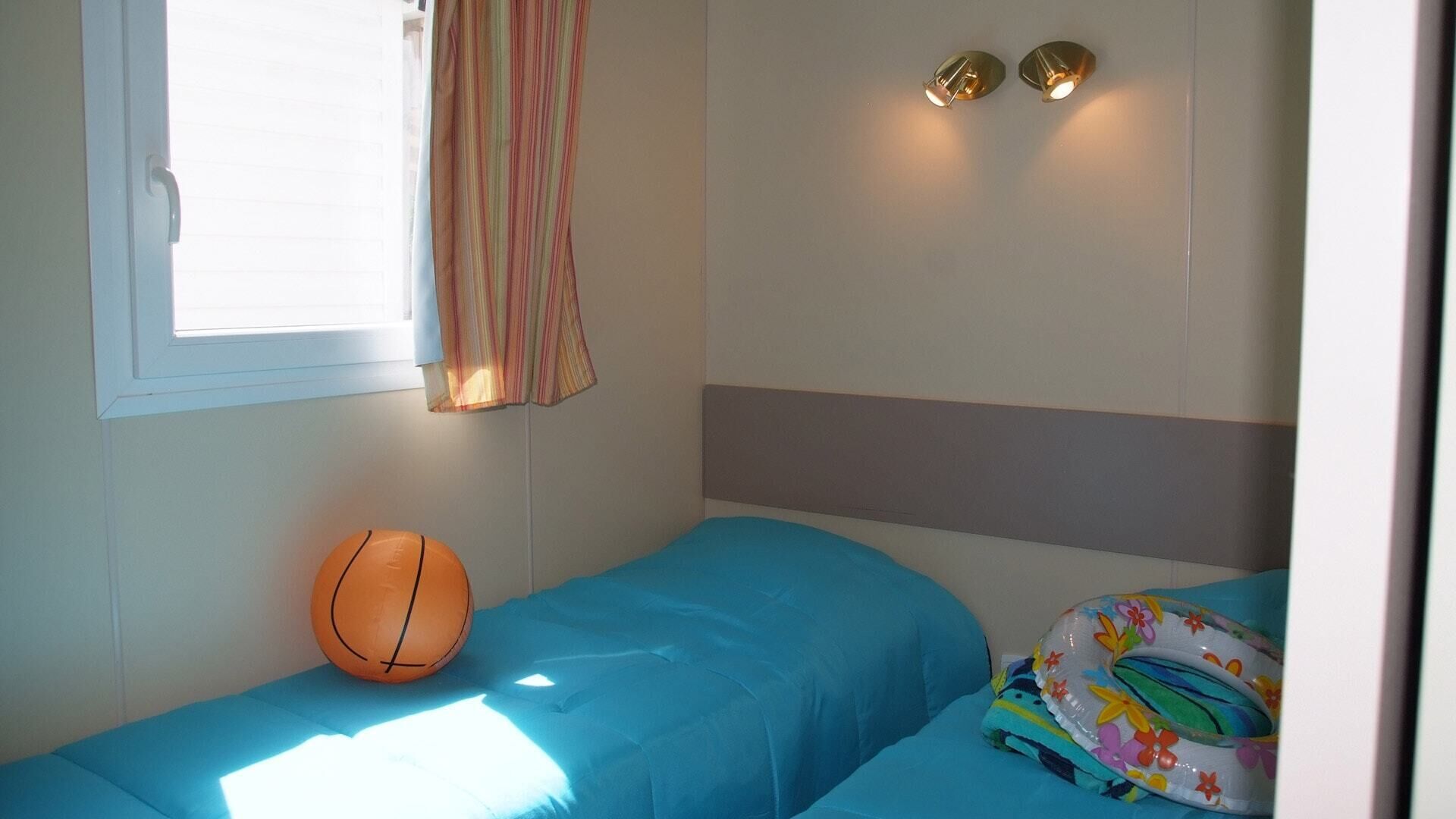 A small, single-bed room with a window, a basketball, and a colorful pillow.