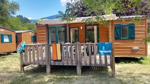 A wooden cabin with a deck, a covered porch, and a visible "IRM" logo. - Camping la Célestine (Beynes)