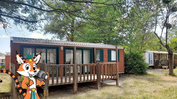 A small cabin with a wooden deck, multiple windows, and a fenced area. - Camping la Célestine (Beynes)