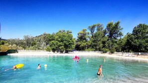 A clear blue pool surrounded by trees and a sandy beach area. - Camping la Célestine (Beynes)