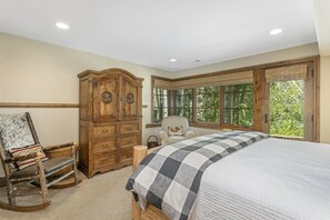 Un dormitorio con una cama grande, un armario de madera, una mecedora y una ventana con vistas a árboles.