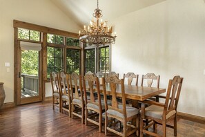 Comedor con mesa y sillas de madera, un candelabro y ventanas amplias con vistas a zonas verdes.