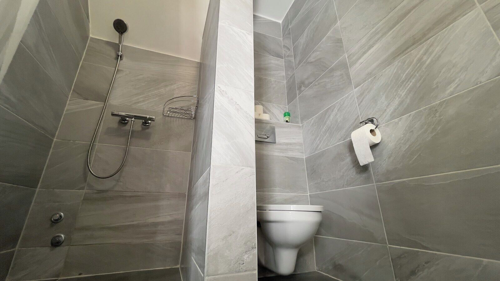 A bathroom with grey tiles, a shower, a toilet, and a hand dryer.
