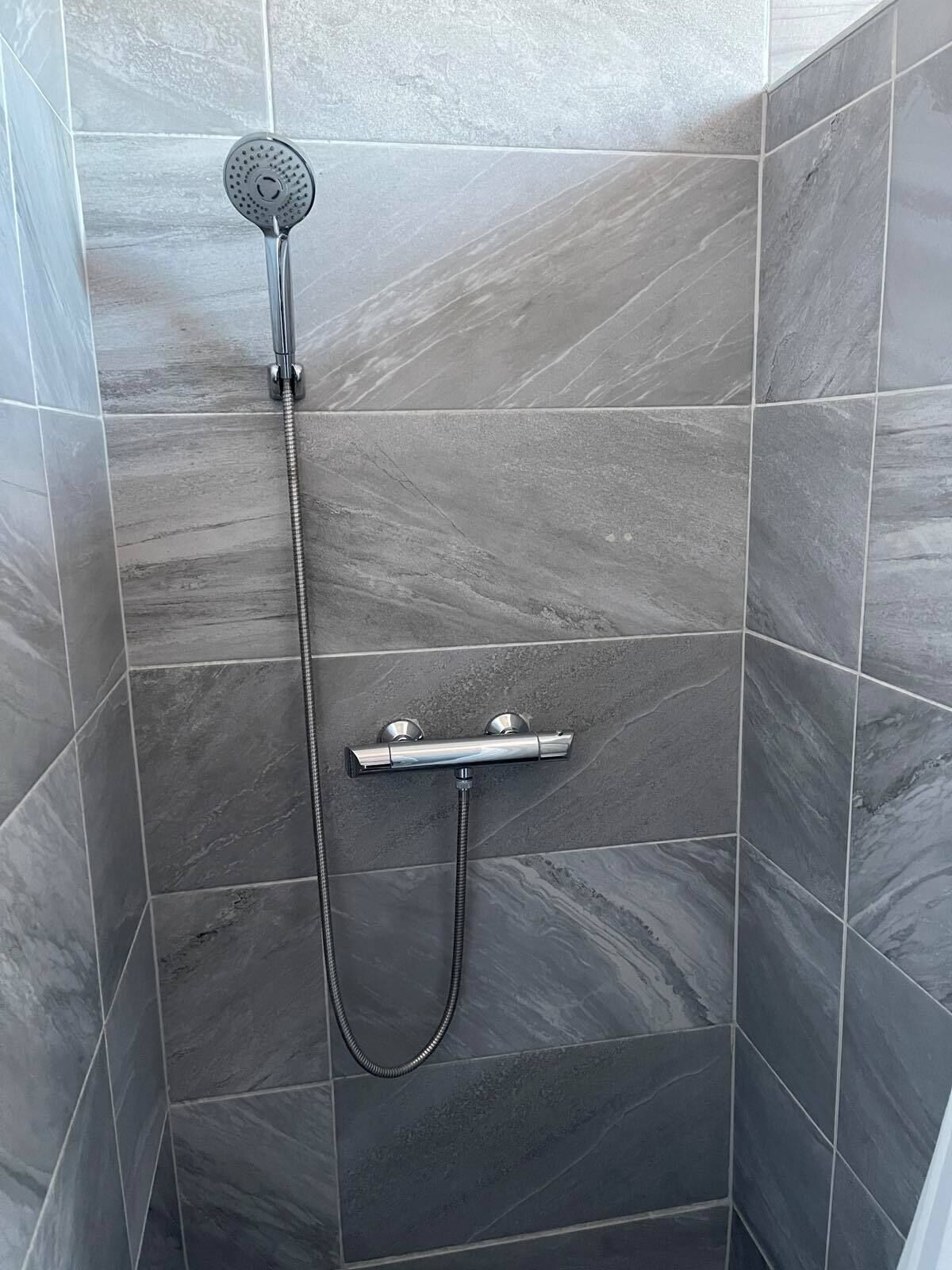 A shower with a handheld showerhead and a handheld shower attachment.