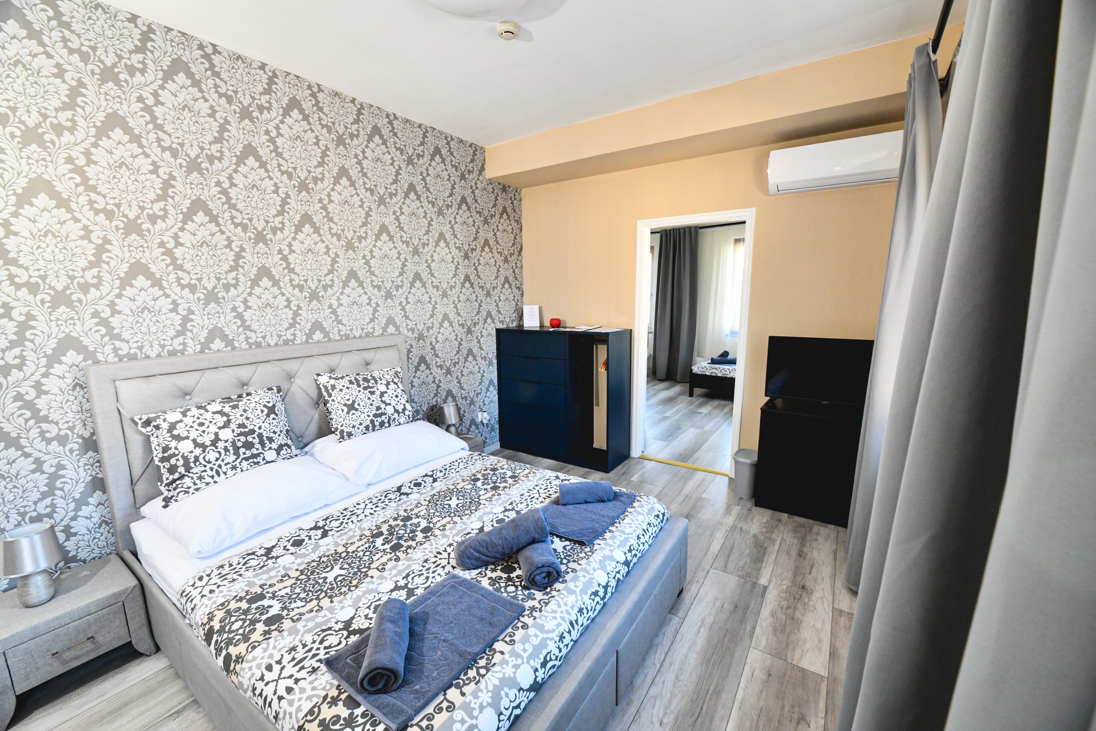 A bedroom with a patterned bedspread, a nightstand, a dresser, and a door leading to another room.